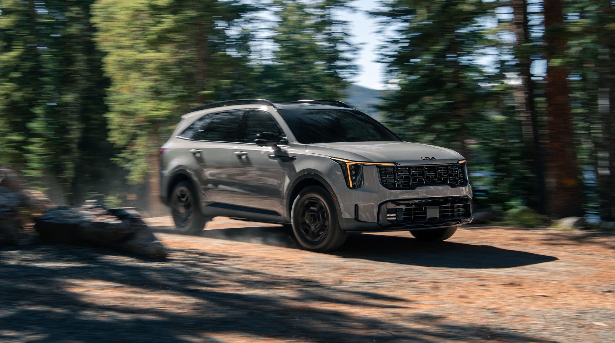 A gray Kia Sorento driving over a dirt Parth through a forest