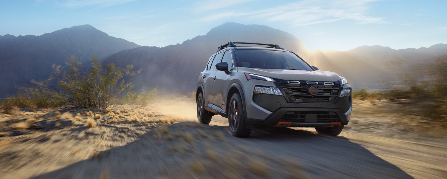 A gray Nissan Rogue driving on a dirt road through a desert