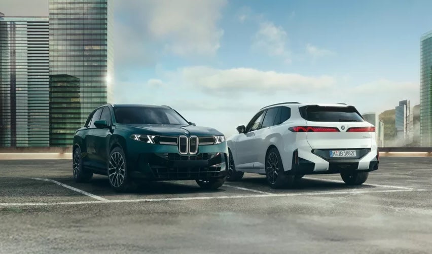 Two BMW SUVs, one green and one white, parked on a city rooftop