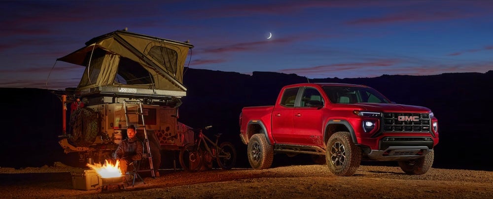 A person camping beside a red GMC truck at night
