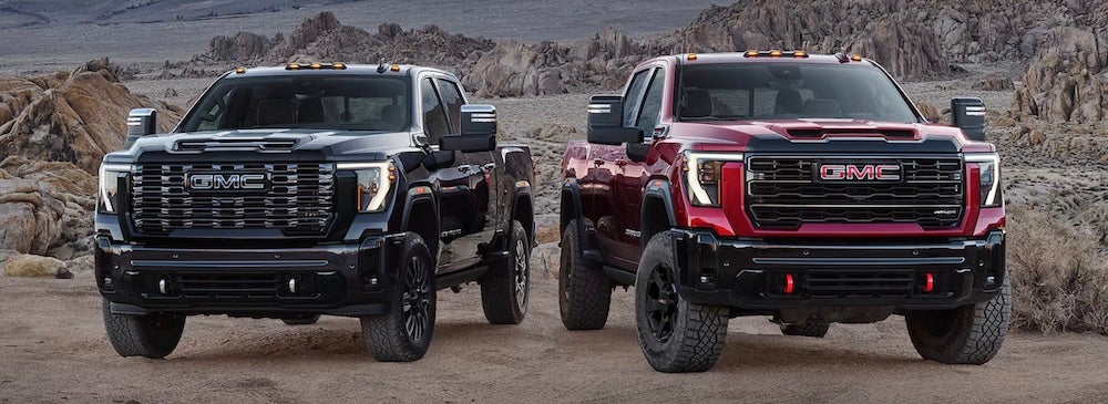 Two GMC Sierra HD pickup trucks, one black and one red, parked in the desert