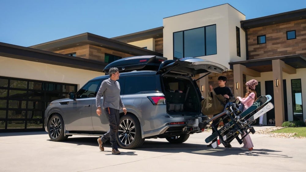 A family unloading ski gear from the trunk of a gray 2026 Infiniti QX80 SUV